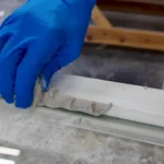 Blue-gloved hand pressing Austin's glazier's putty into a window sash rabbet