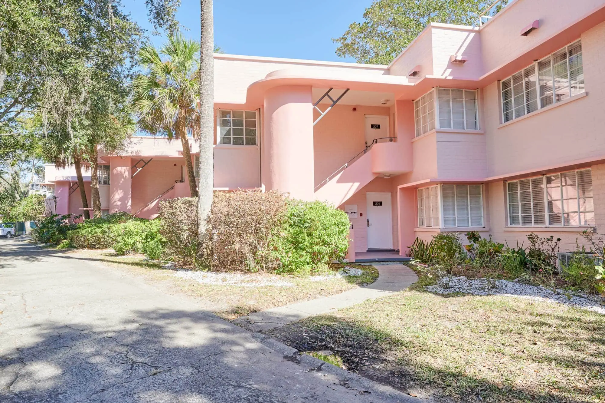 Pink multi-story apartment building with large windows, surrounded by trees and shrubbery.